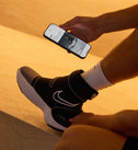 Persoon met de Hyperboot by Nike × Hyperice aan en een smartphone in de hand