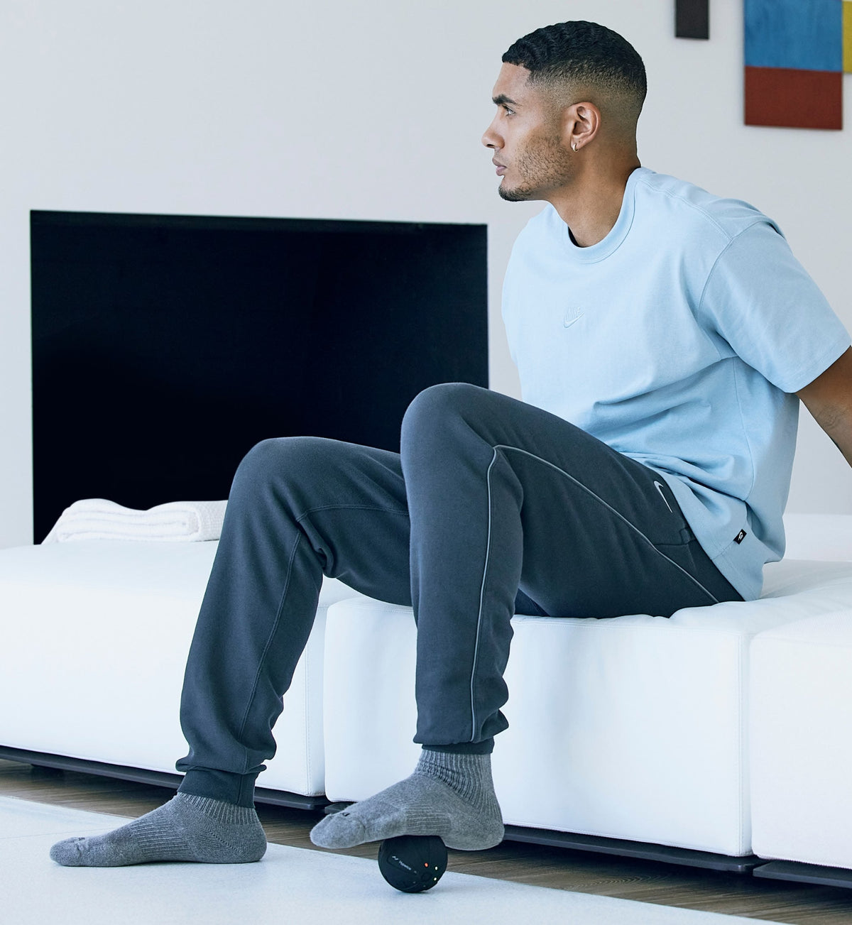 Man sitting on a white couch in a modern living room using a Hypersphere go on his foot.