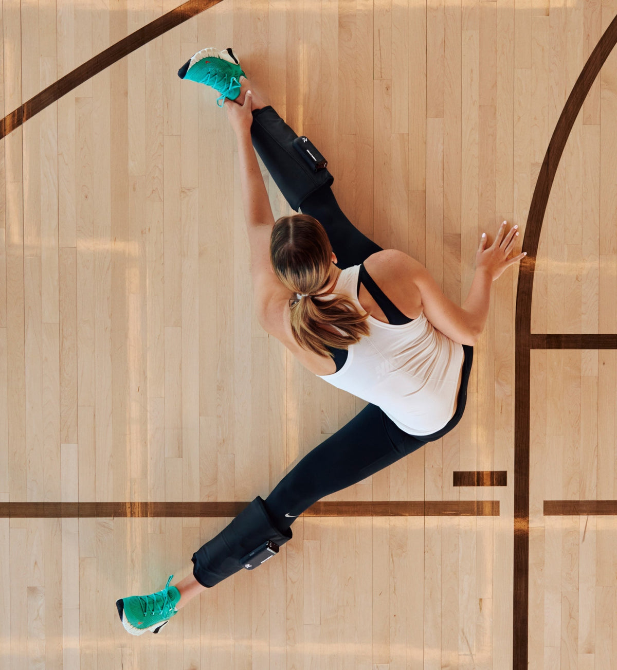 Woman stretching on a basketball court wearing Normatec Lower Legs